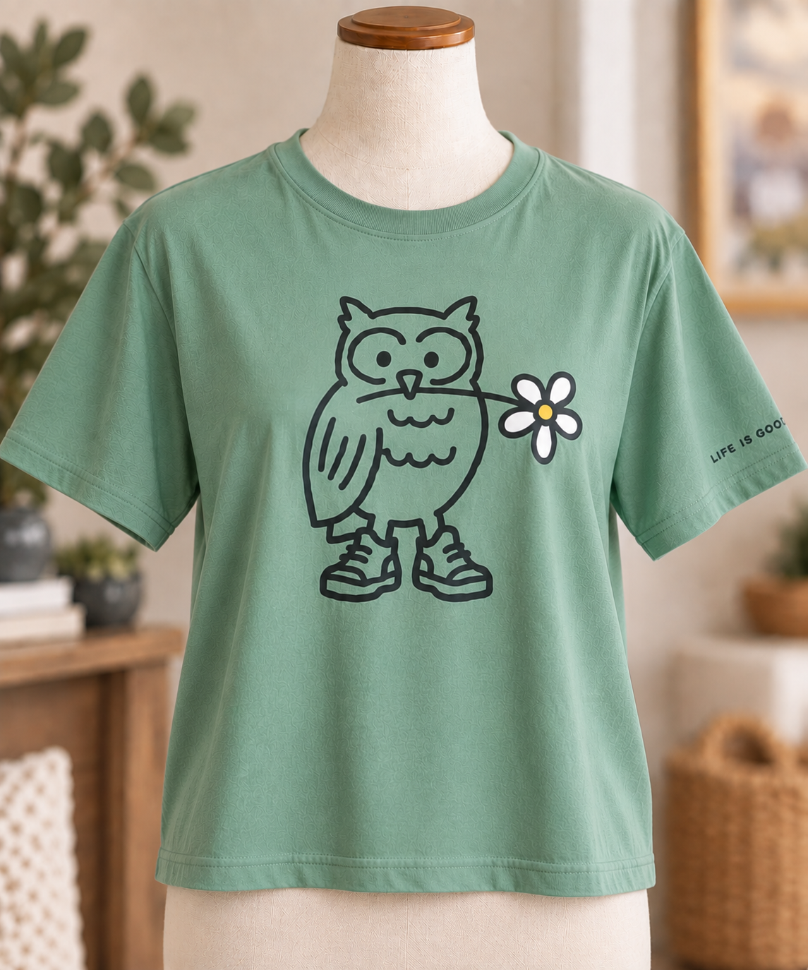 Life is Good women’s green boxy-fit T-shirt featuring an owl holding a daisy, displayed on a torso mannequin.