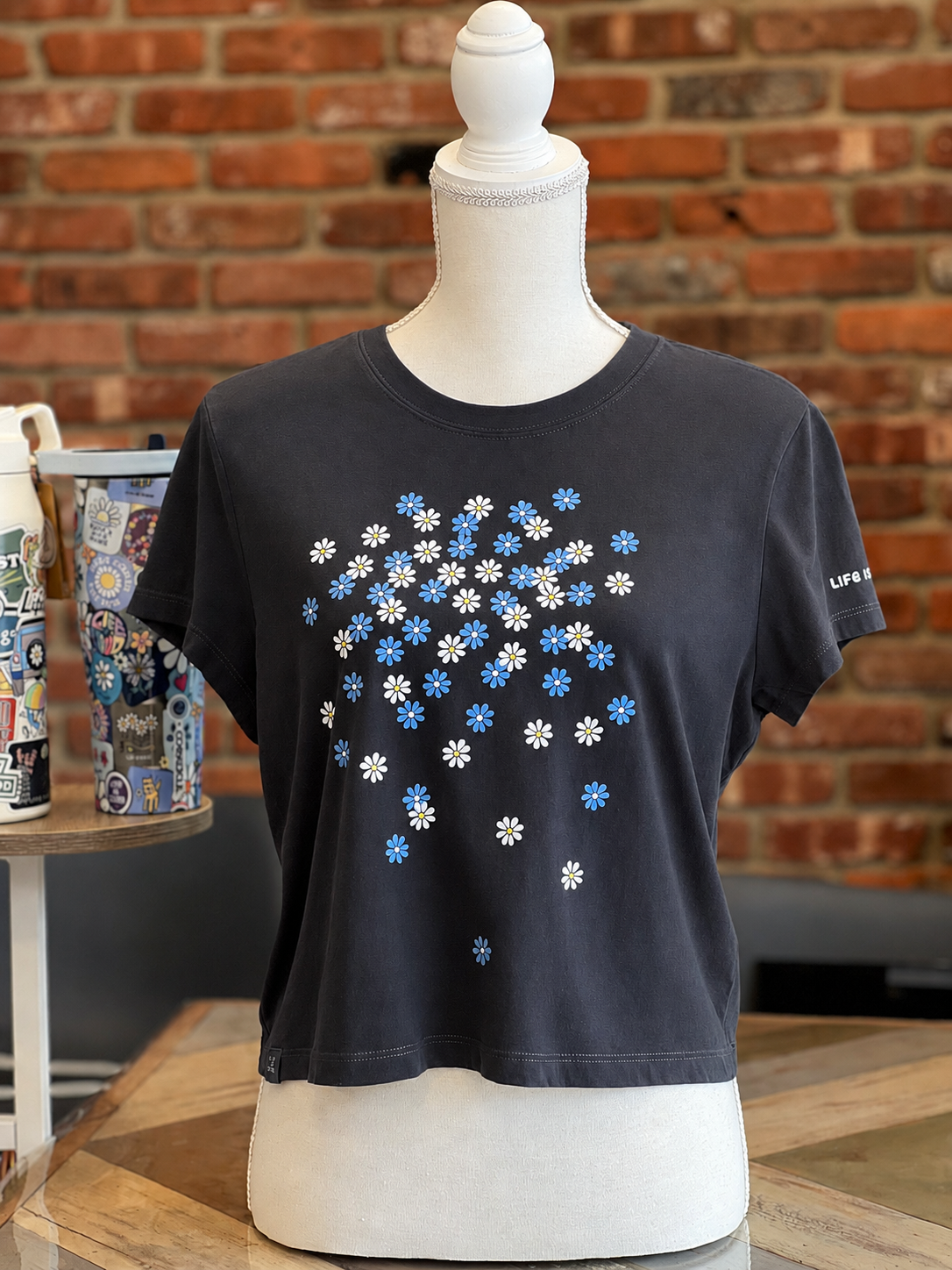 Life is Good women’s faded black T-shirt with scattered blue and white daisy print.
