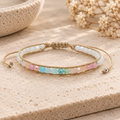 Lotus and Luna Coconut Crush bracelet with pastel multicolor and white beads on tan adjustable cord, displayed on a neutral stone surface.