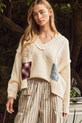 Woman wearing Oddi ivory V-neck knit sweater with crochet appliqués and mixed-fabric patchwork details.