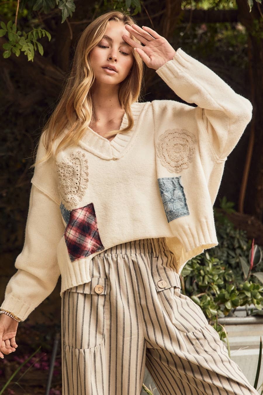 Woman wearing Oddi ivory V-neck knit sweater with crochet appliqués and mixed-fabric patchwork details.